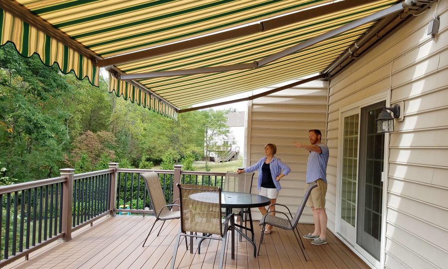 Green and cream striped retractable awning shading a backyard deck with a couple admiring it
